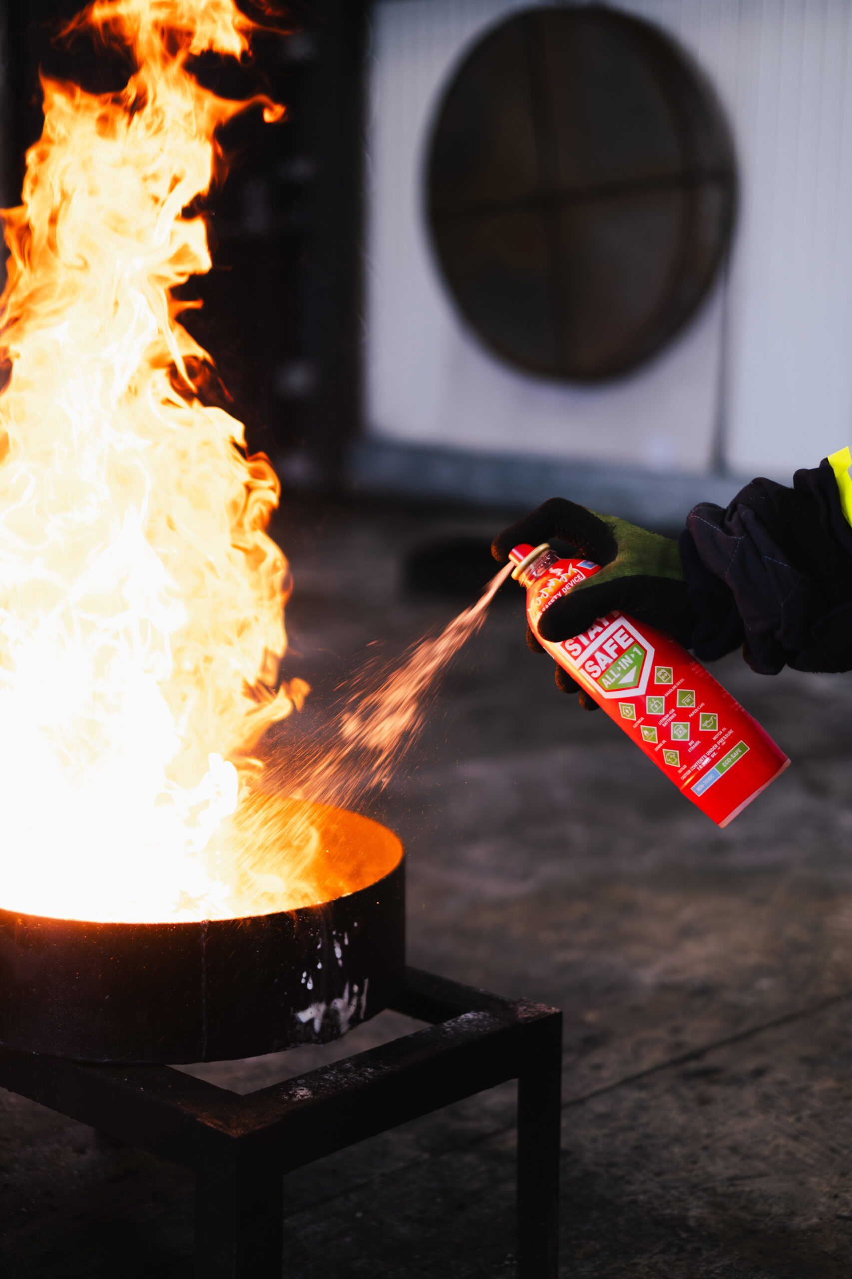 Person spraying a red LifeSafe extinguisher at flames in a metal container during a test.
