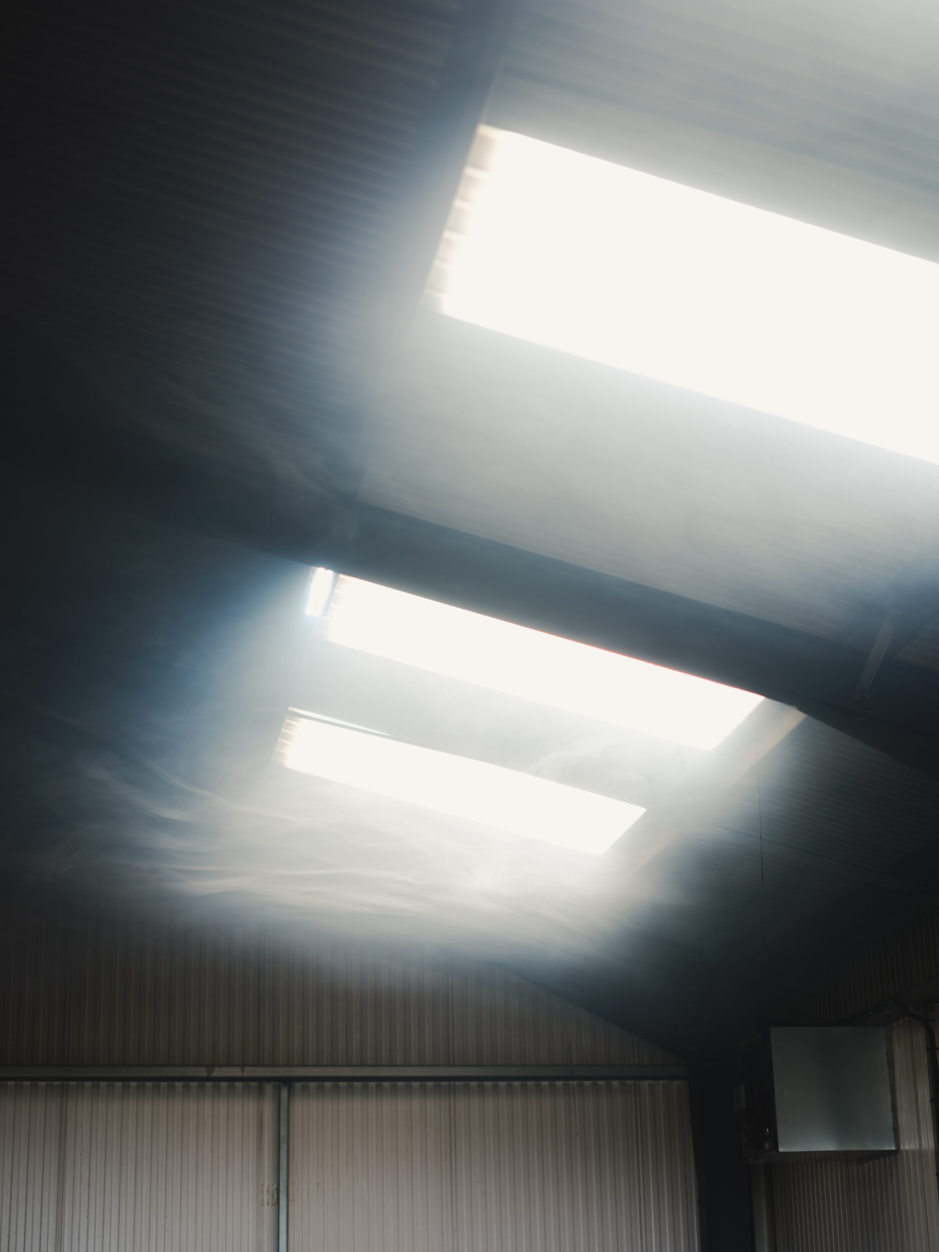 Light streaming down through skylights into a smoke-filled warehouse.