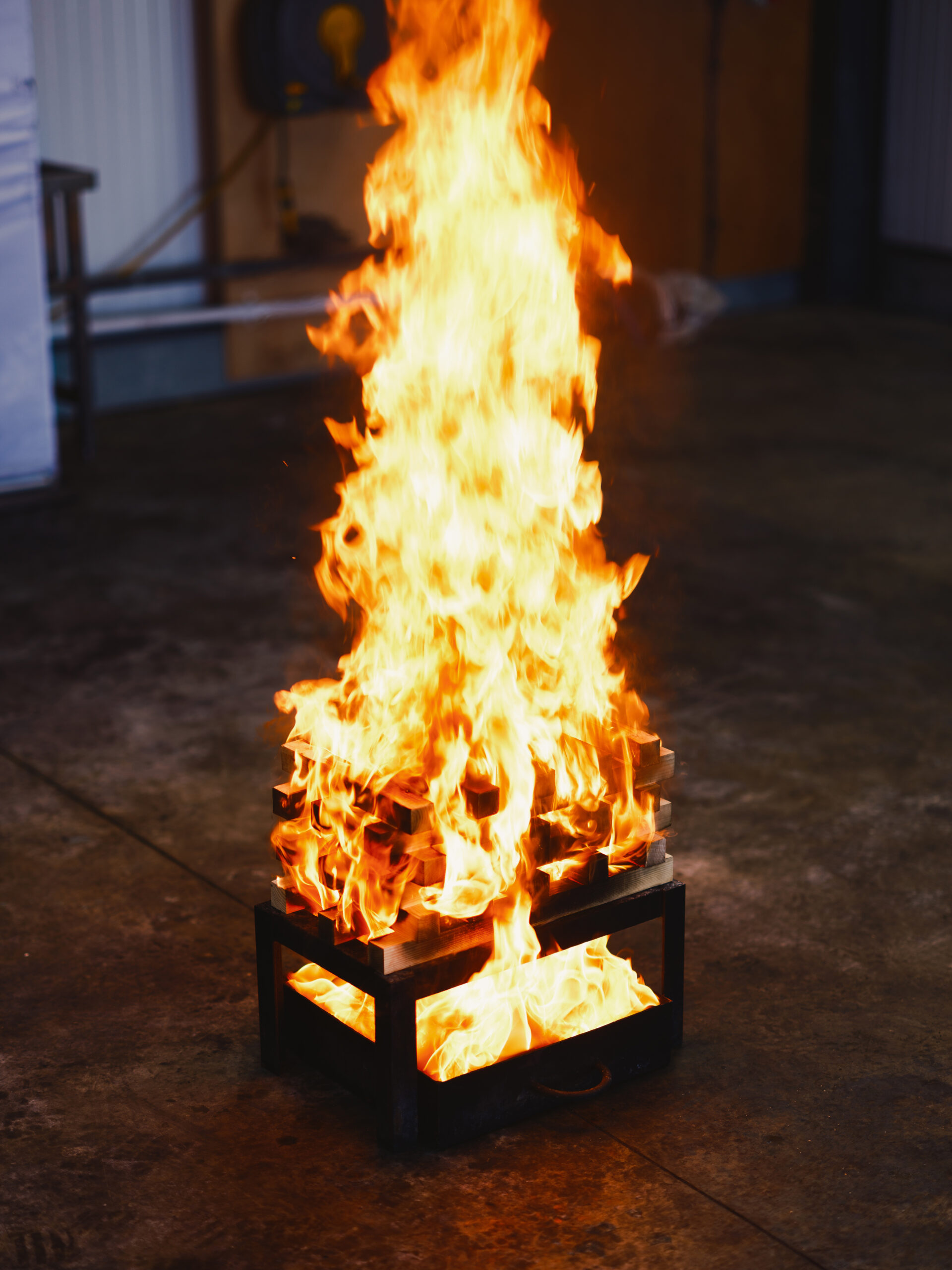 Close-up of a wooden block fire burning inside a metal testing container.